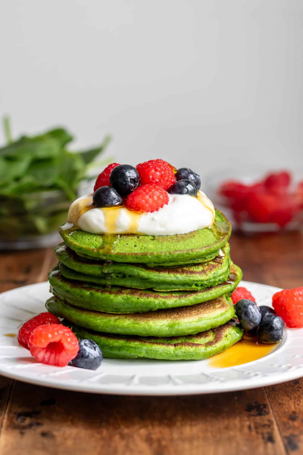 Stack of spinach pancakes topped with yogurt, raspberries, blueberries and maple syrup.