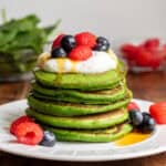 Stack of spinach pancakes topped with yogurt, raspberries, blueberries and maple syrup.