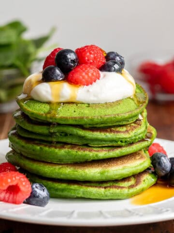 Stack of spinach pancakes topped with yogurt, raspberries, blueberries and maple syrup.