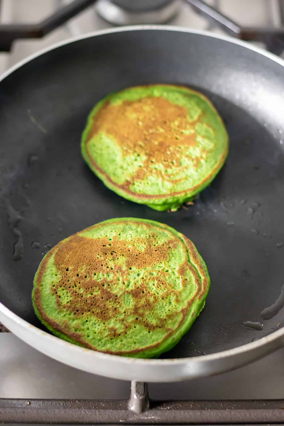 Flipped spinach pancakes in a frying pan.
