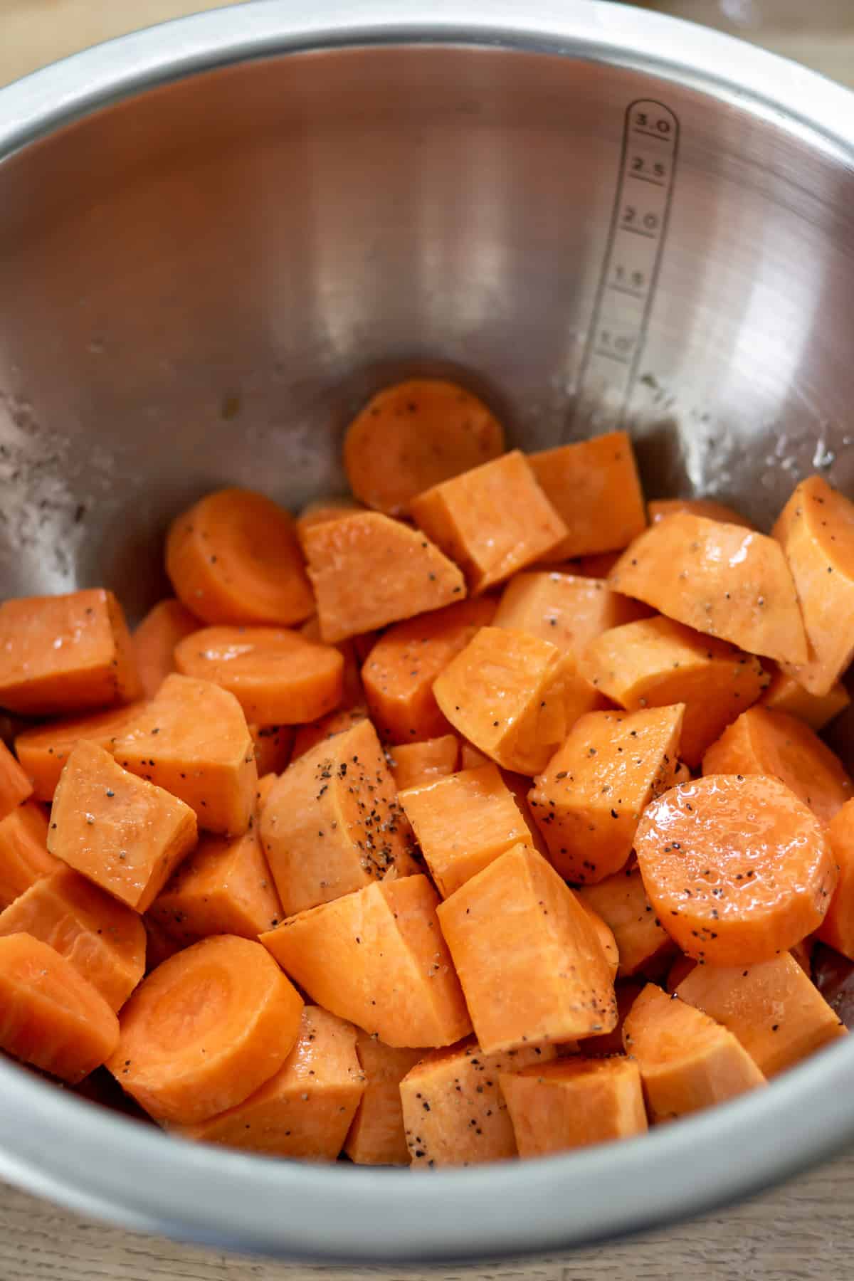 Sweet potatoes and carrots in a bowl with oil and seasonings.