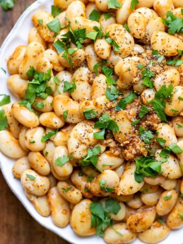 Close up of a plate of garlic butter beans topped with fresh parsley.