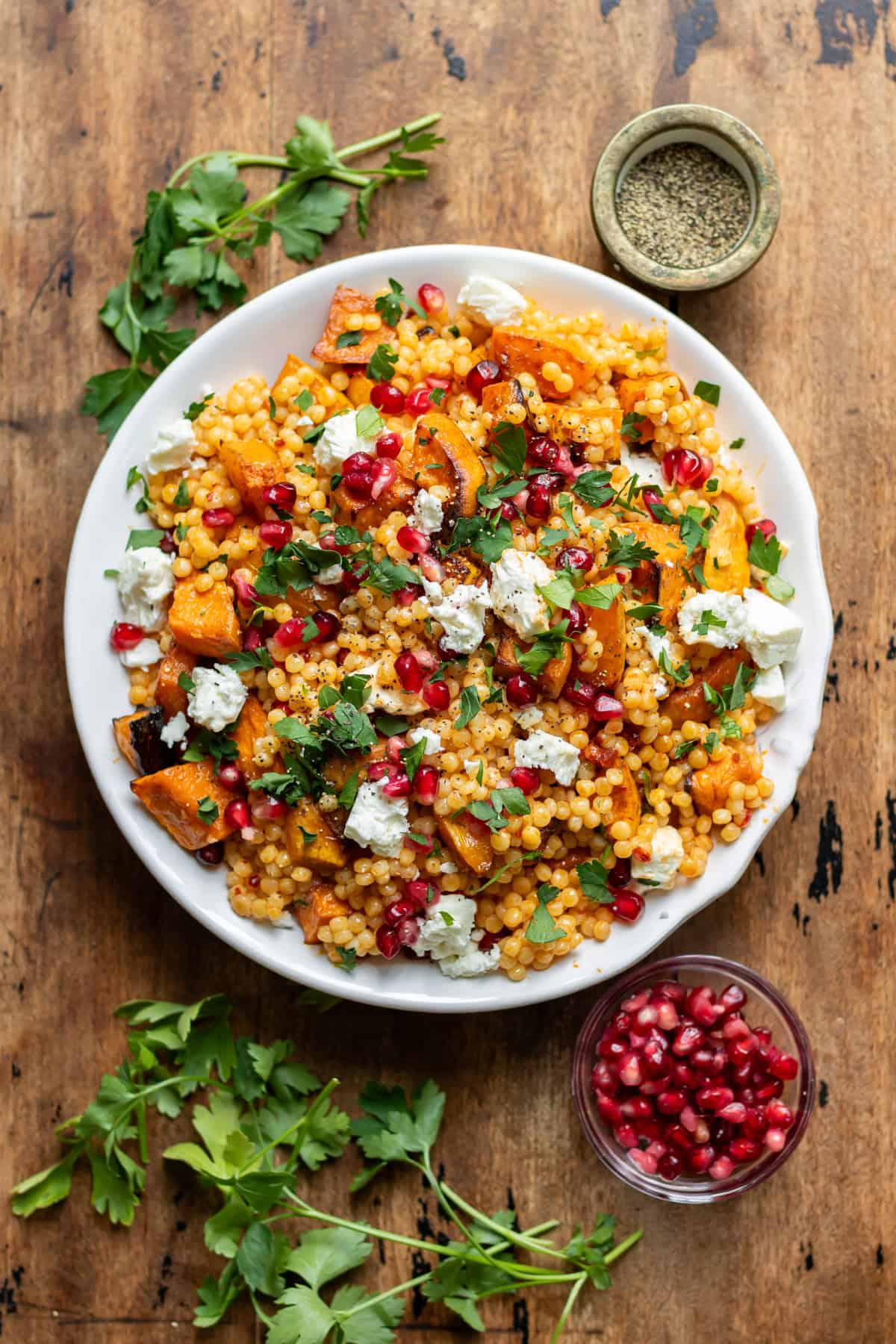 Wooden table with a dish of giant pearl couscous with roasted vegetables.
