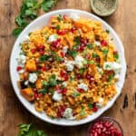 Wooden table with a dish of giant pearl couscous with roasted vegetables.