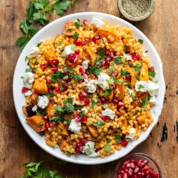 Wooden table with a dish of giant pearl couscous with roasted vegetables.
