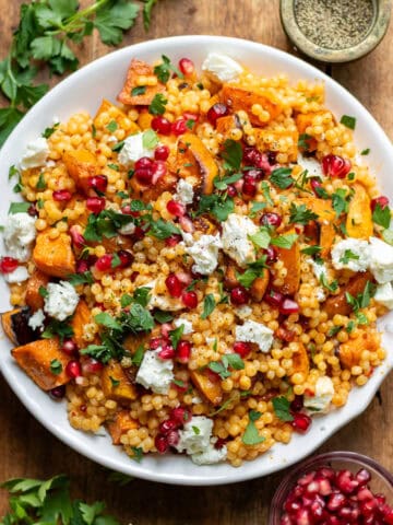 Wooden table with a dish of giant pearl couscous with roasted vegetables.
