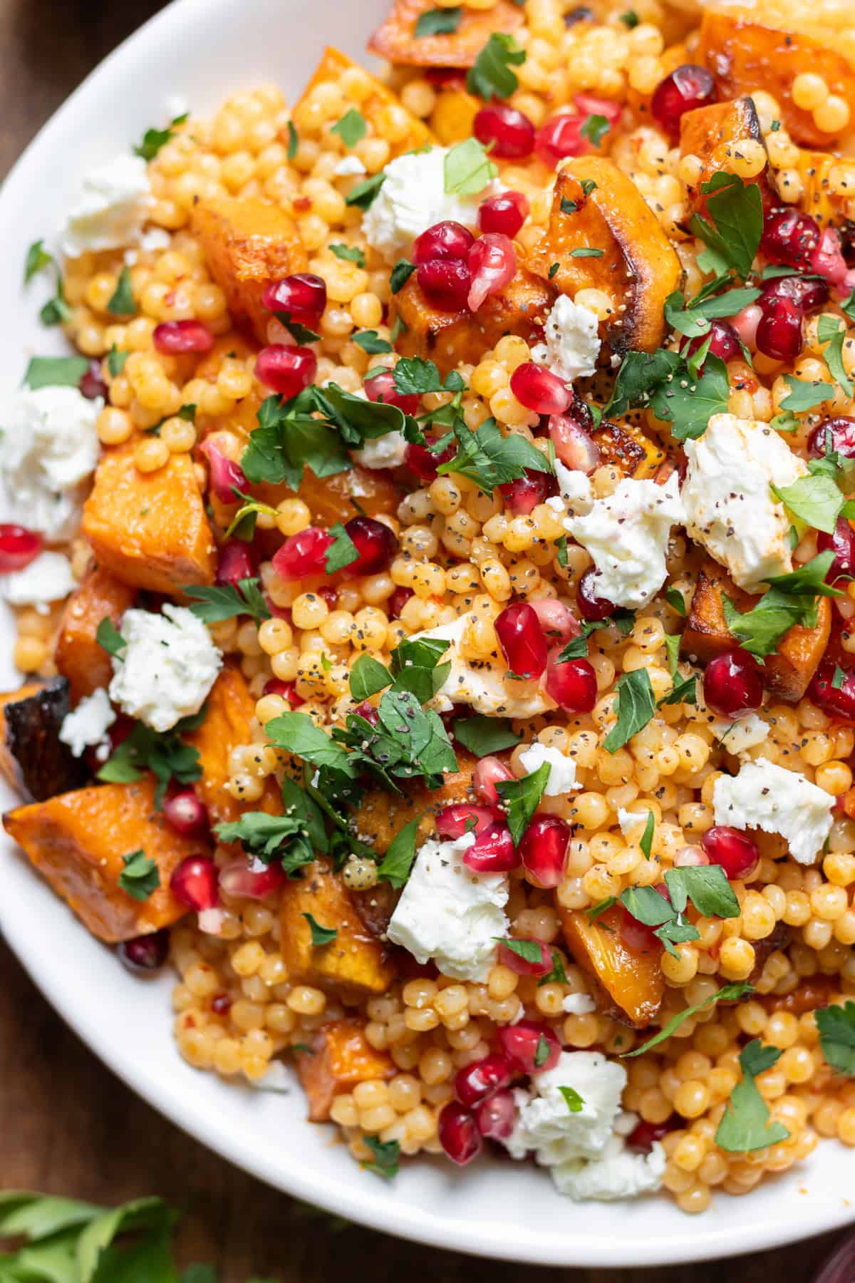 Close up of a bowl of harissa pearl couscous salad with roasted vegetables, feta and pomegranate seeds.