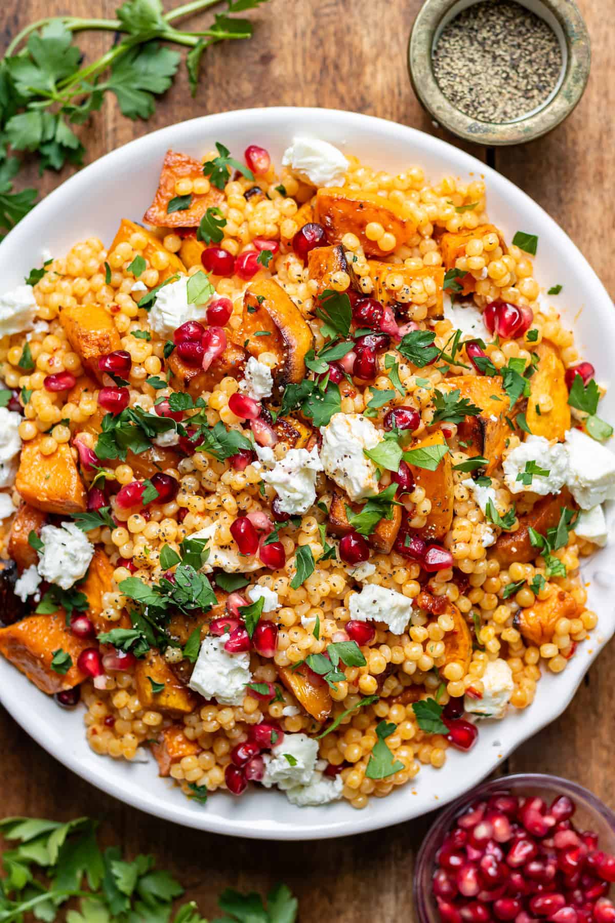 Looking down at a bowl of giant couscous salad with roasted vegetables, feta and pomegranate.