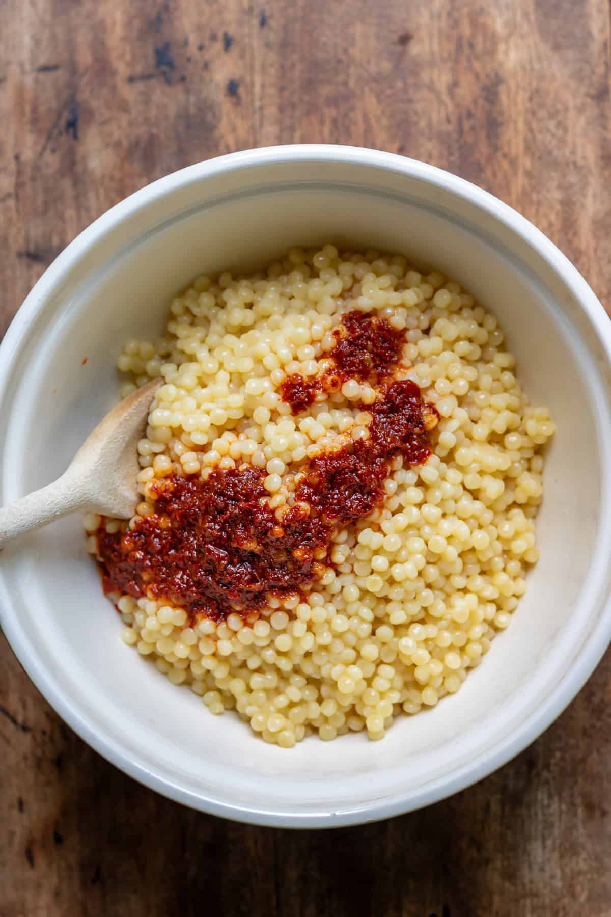 Stirring the harissa oil into the giant couscous.