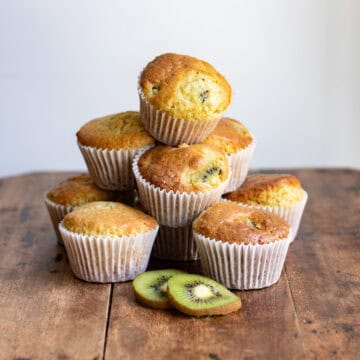 A pile of kiwi muffins, next to slices of kiwi.