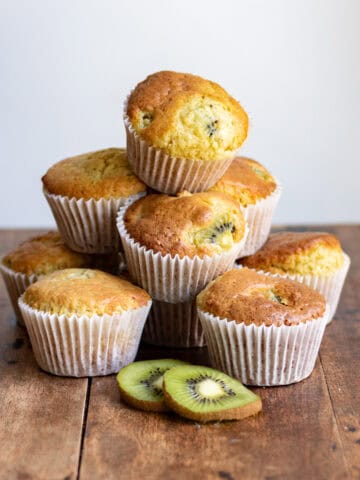 A pile of kiwi muffins, next to slices of kiwi.