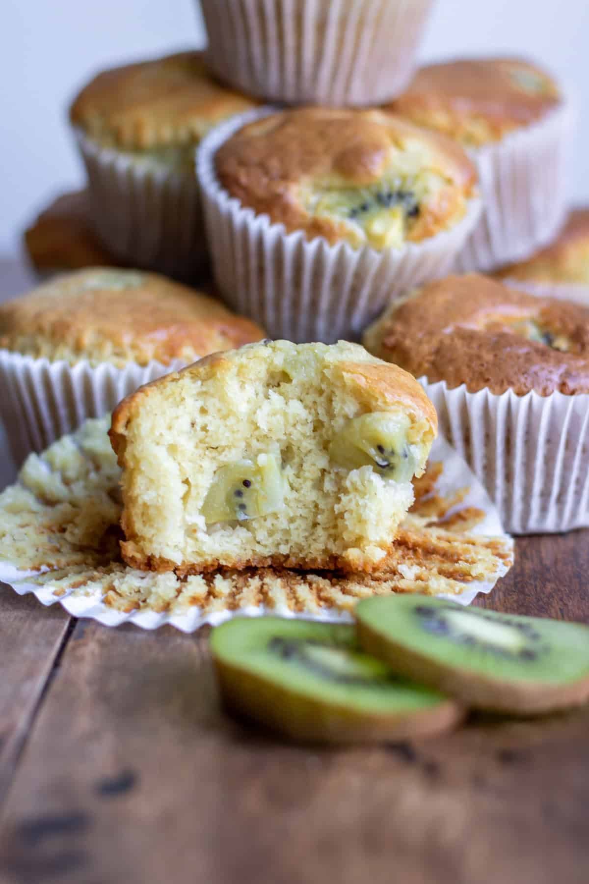 A kiwi muffin with a bite out, in front of other muffins.