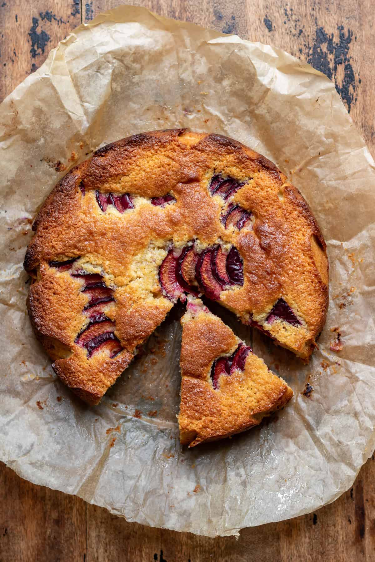 Looking down at an almond plum cake with a slice missing and one pulled out slightly.
