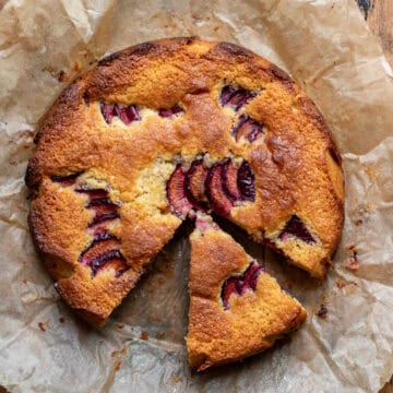 Looking down at an almond plum cake with a slice missing and one pulled out slightly.