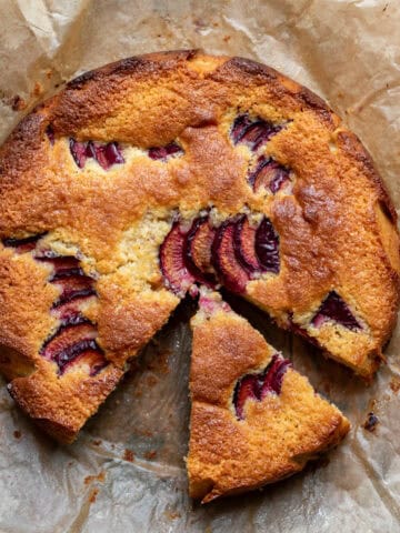 Looking down at an almond plum cake with a slice missing and one pulled out slightly.