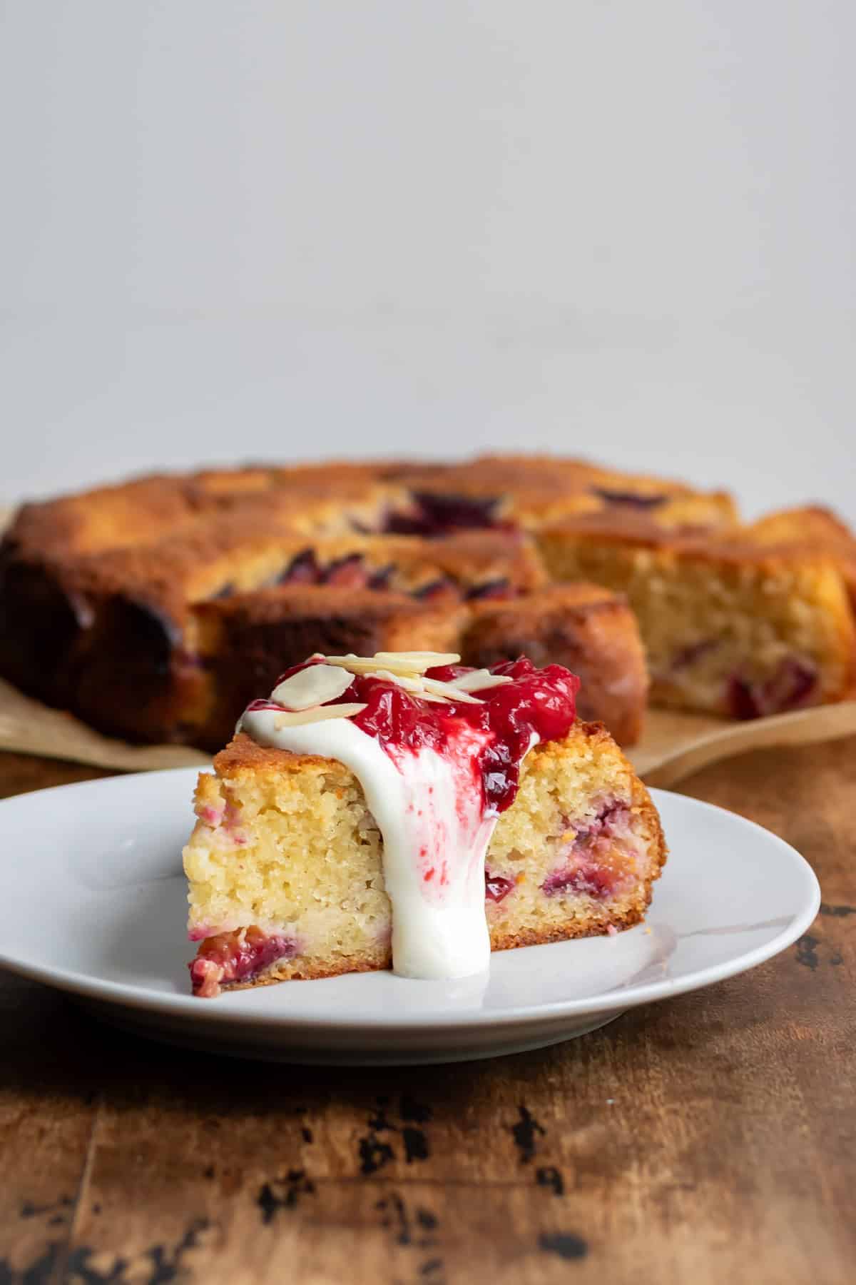 A slice of almond plum cake topped with vanilla plum sauce and sweet sour cream.