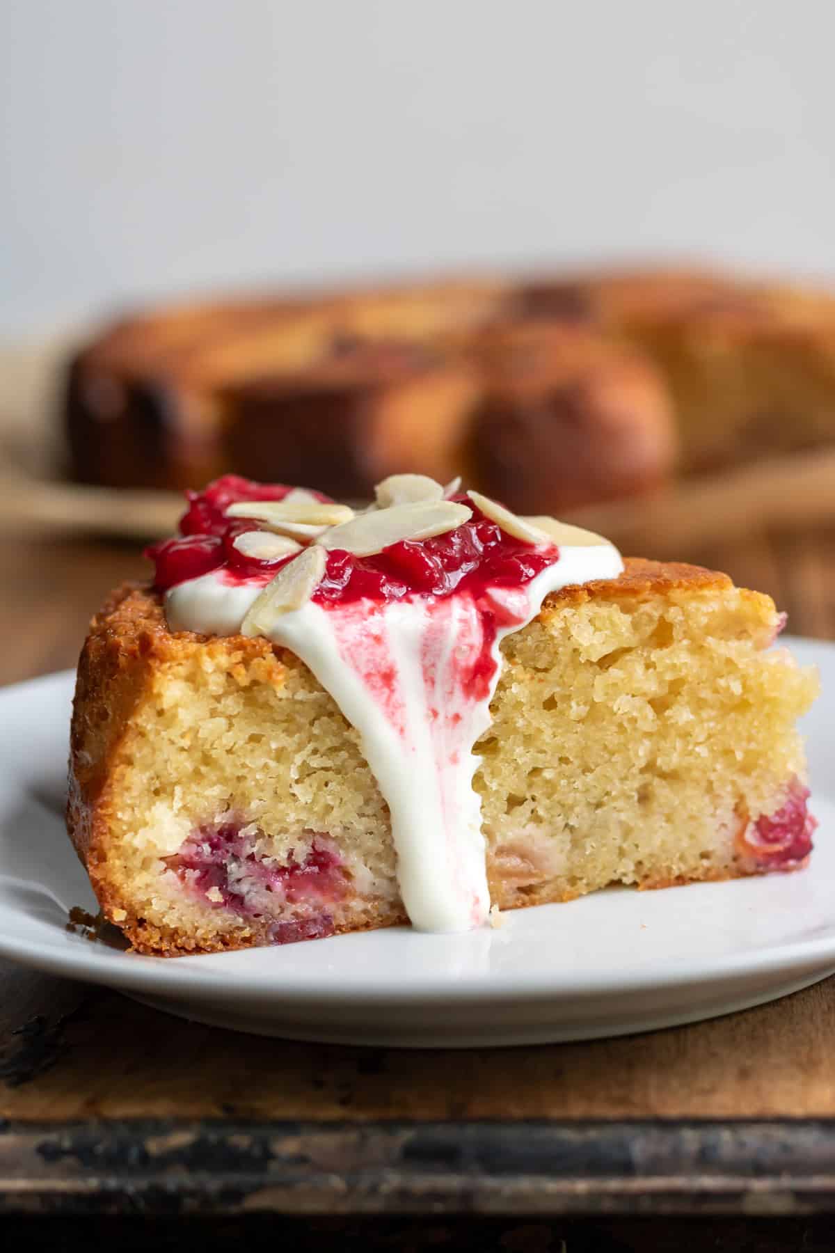 Close up of a slice of almond plum cake topped with vanilla plum sauce and sweet sour cream.
