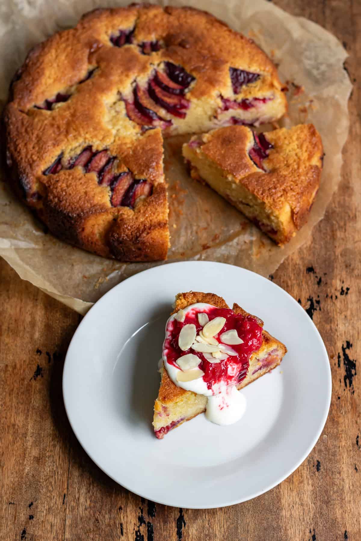 Looking down at an almond plum cake, plus a slice of it on a plate.