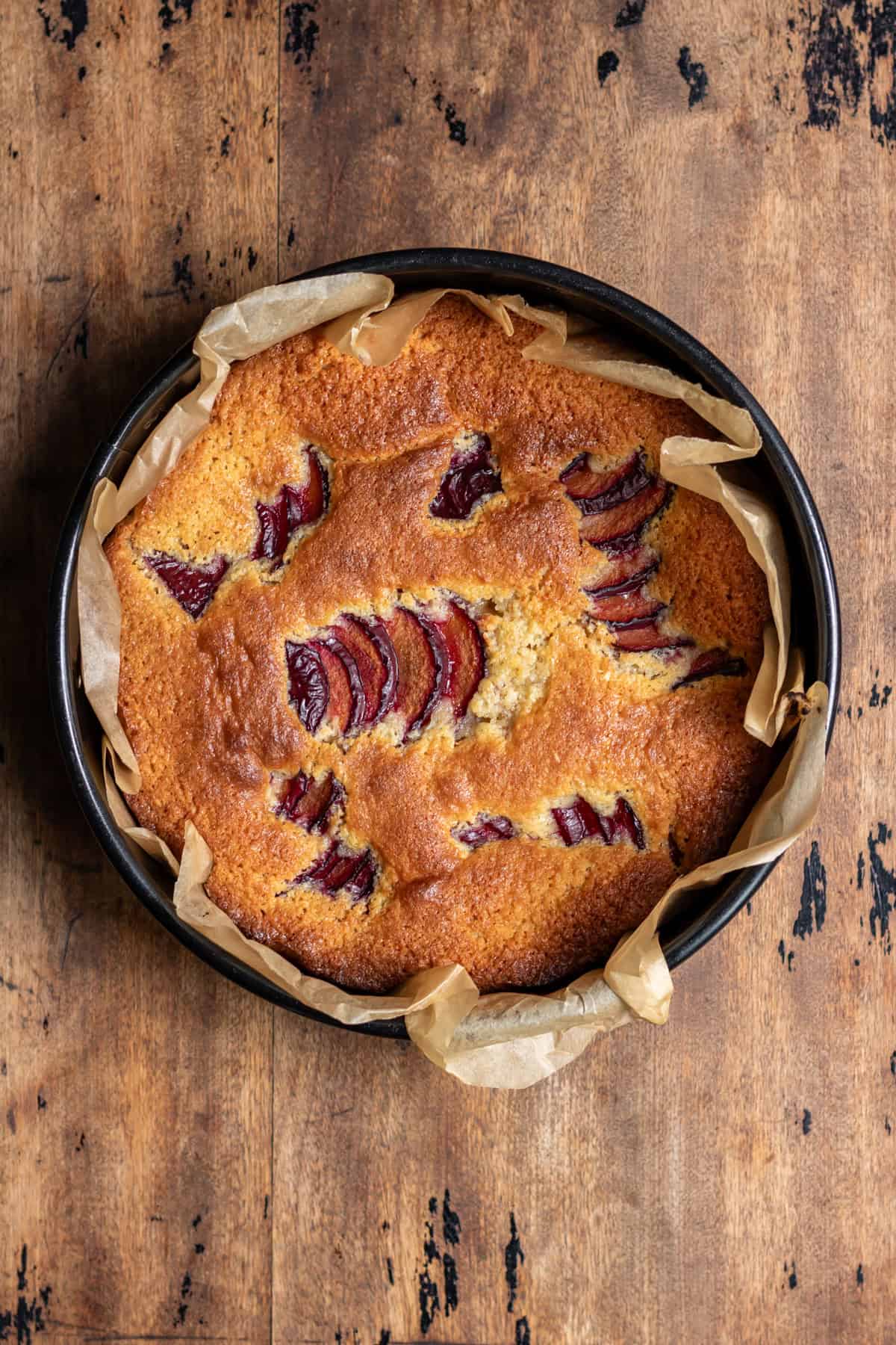 A cooked almond plum cake in the pan on a wooden table.