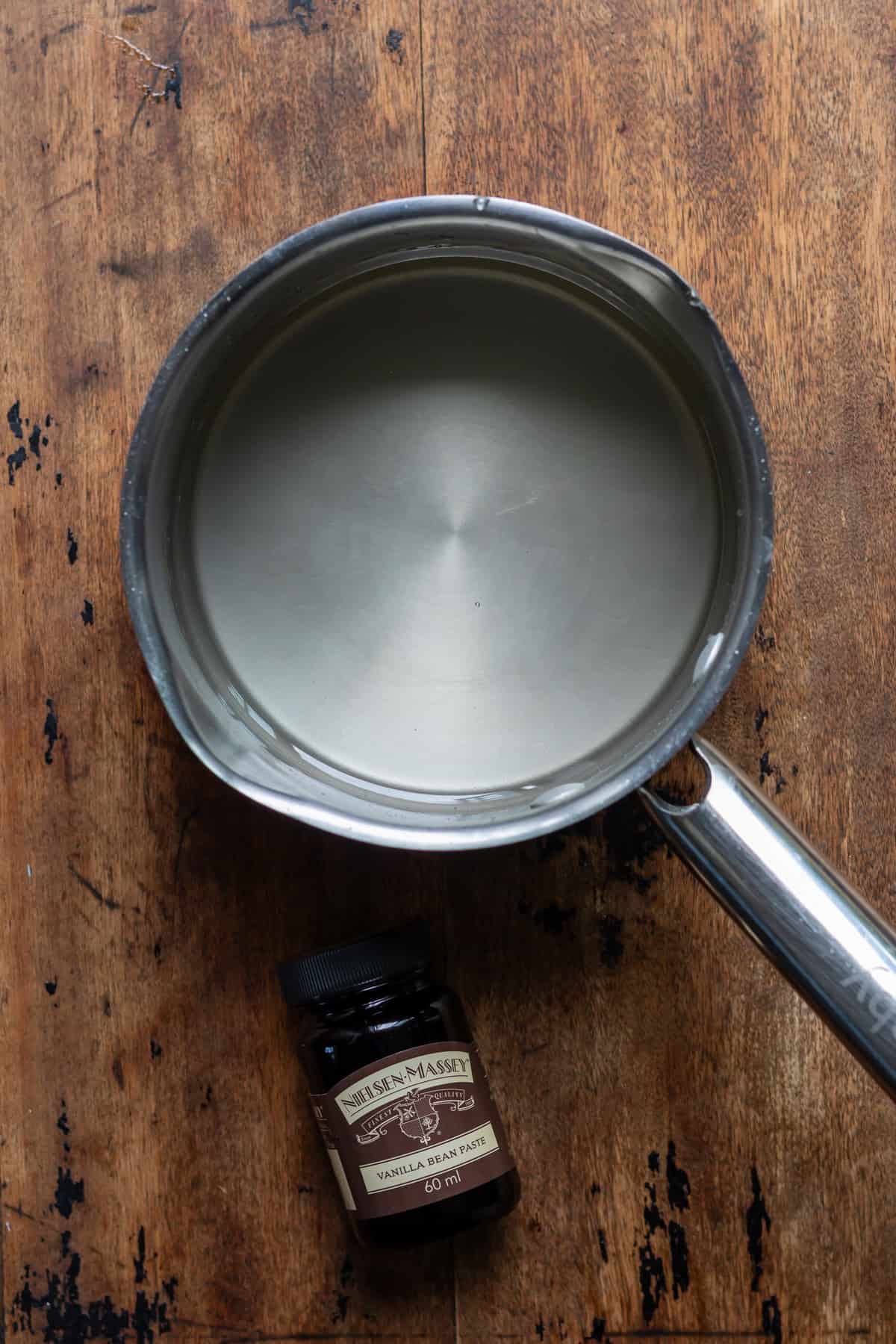Saucepan of simple syrup next to a bottle of vanilla bean paste.