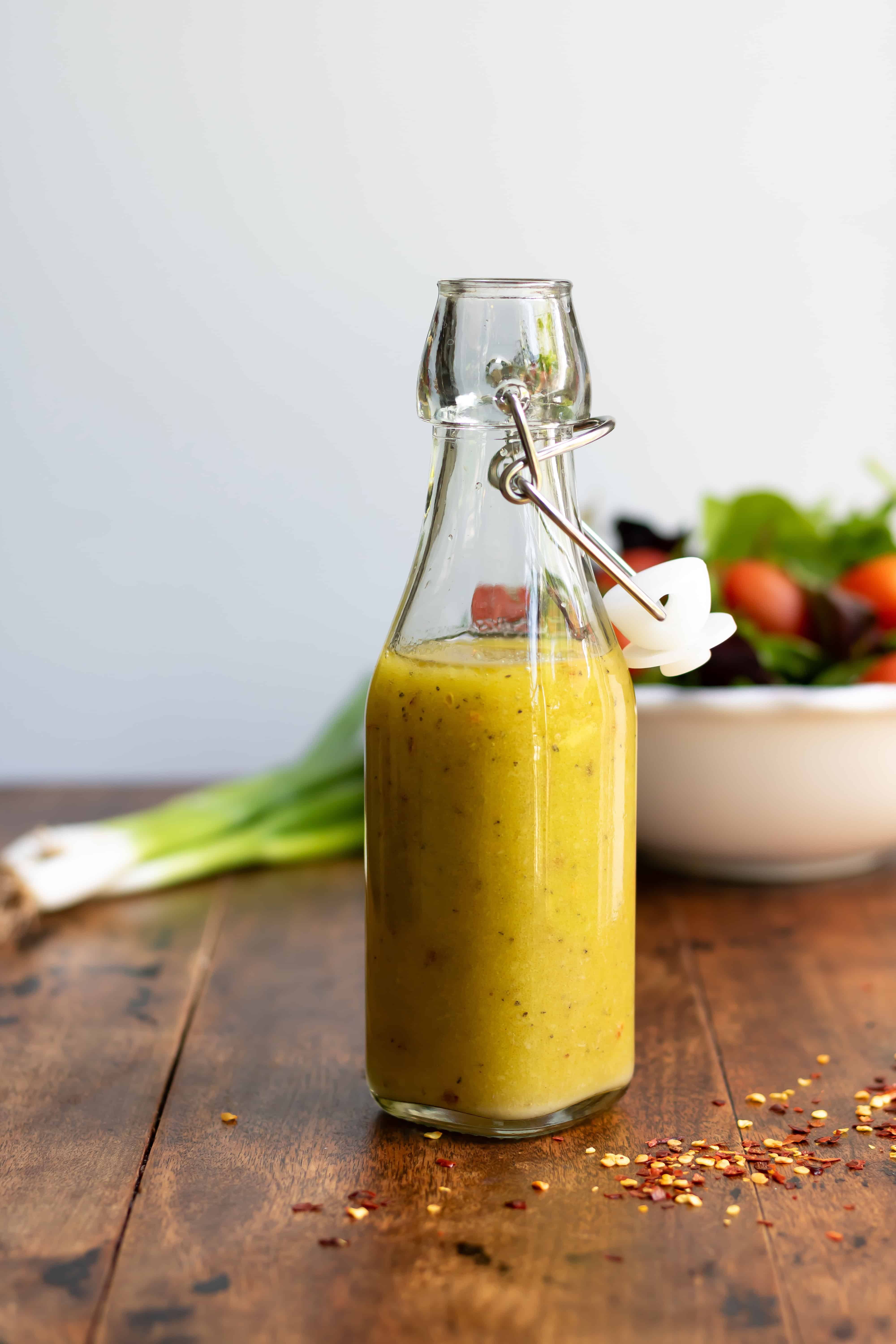 Glass bottle of hot honey vinaigrette dressing in front of a bowl of salad.