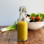 Glass bottle of hot honey vinaigrette dressing in front of a bowl of salad.
