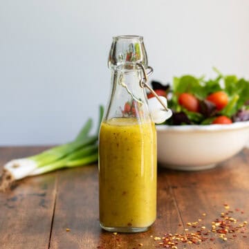Glass bottle of hot honey vinaigrette dressing in front of a bowl of salad.