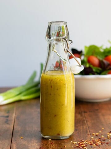 Glass bottle of hot honey vinaigrette dressing in front of a bowl of salad.