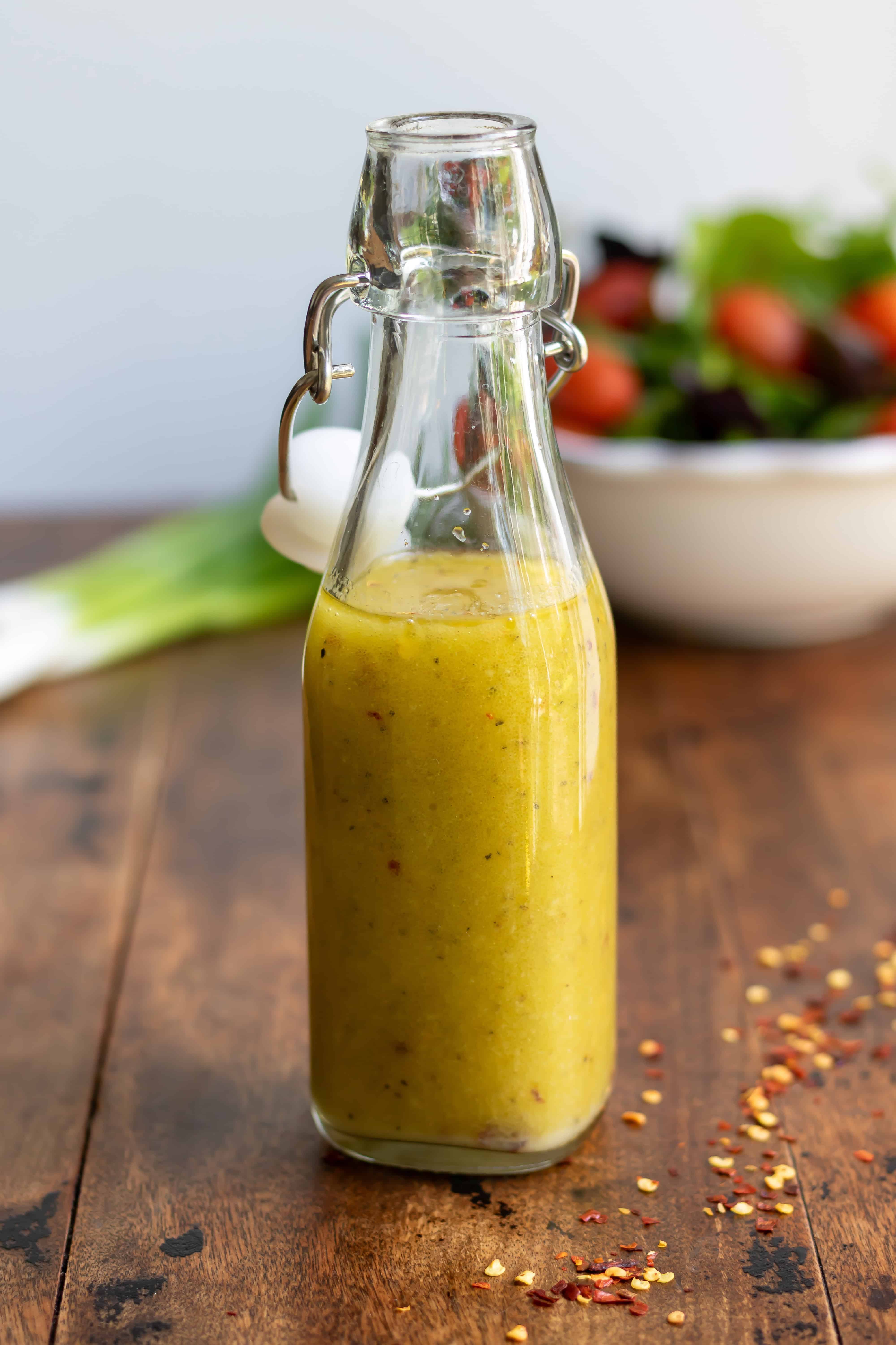 Glass bottle of hot honey vinaigrette dressing in front of a bowl of salad.