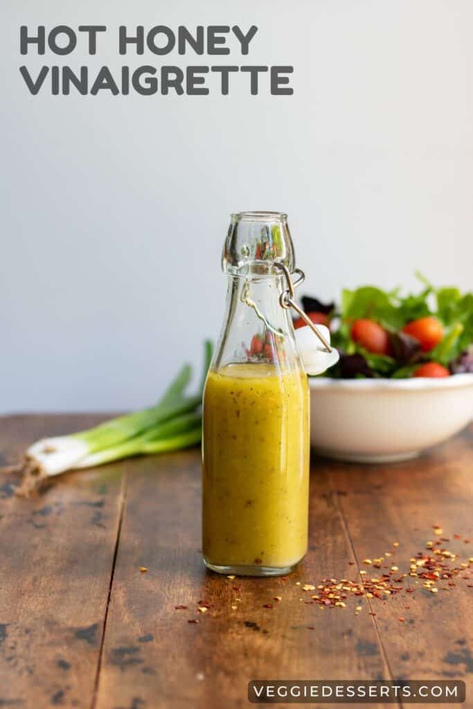 Bottle of hot honey vinaigrette in front of bowl of salad with text: Hot Honey Vinaigrette.
