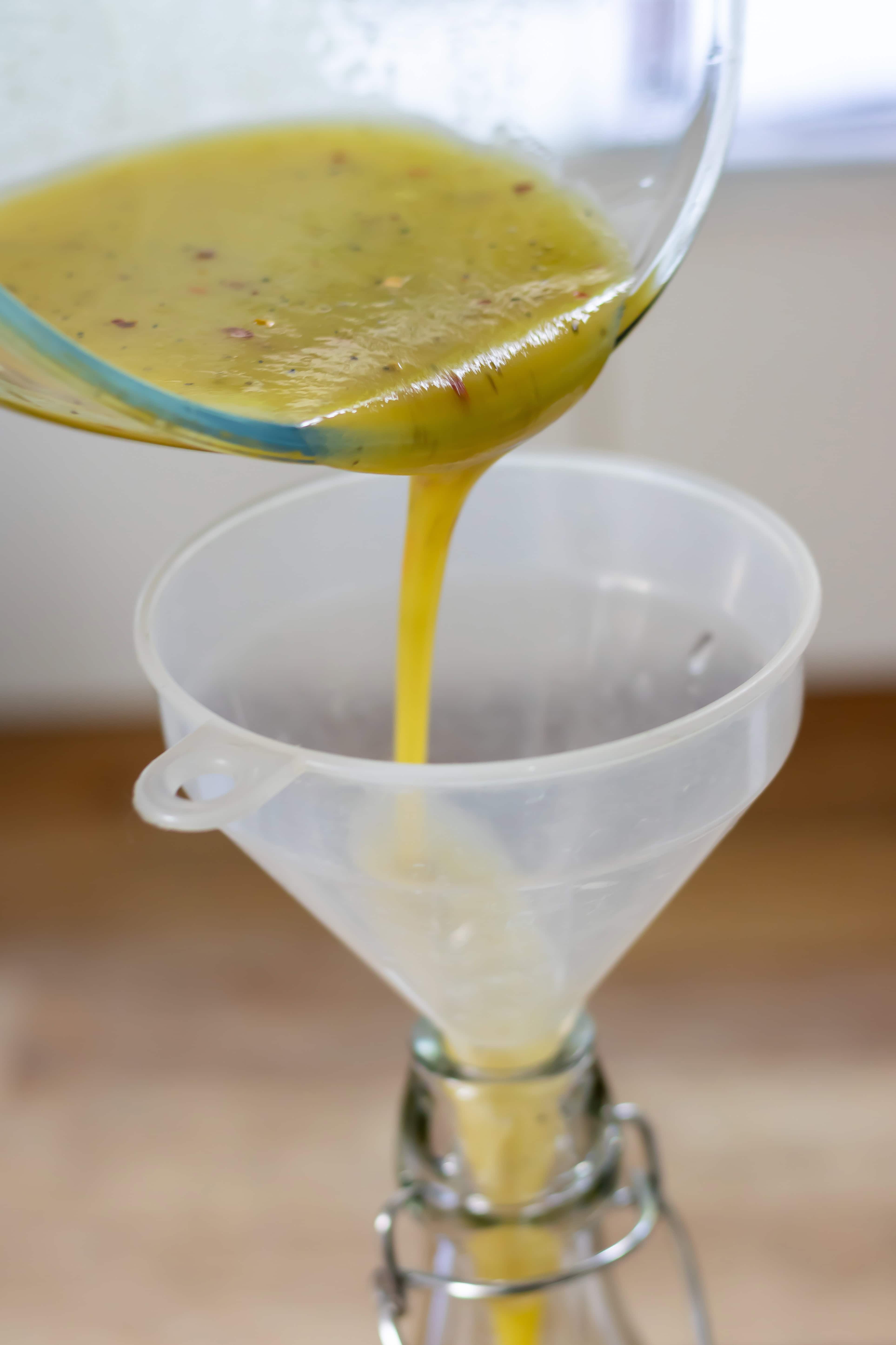 Pouring the hot honey vinaigrette into a bottle via a funnel.