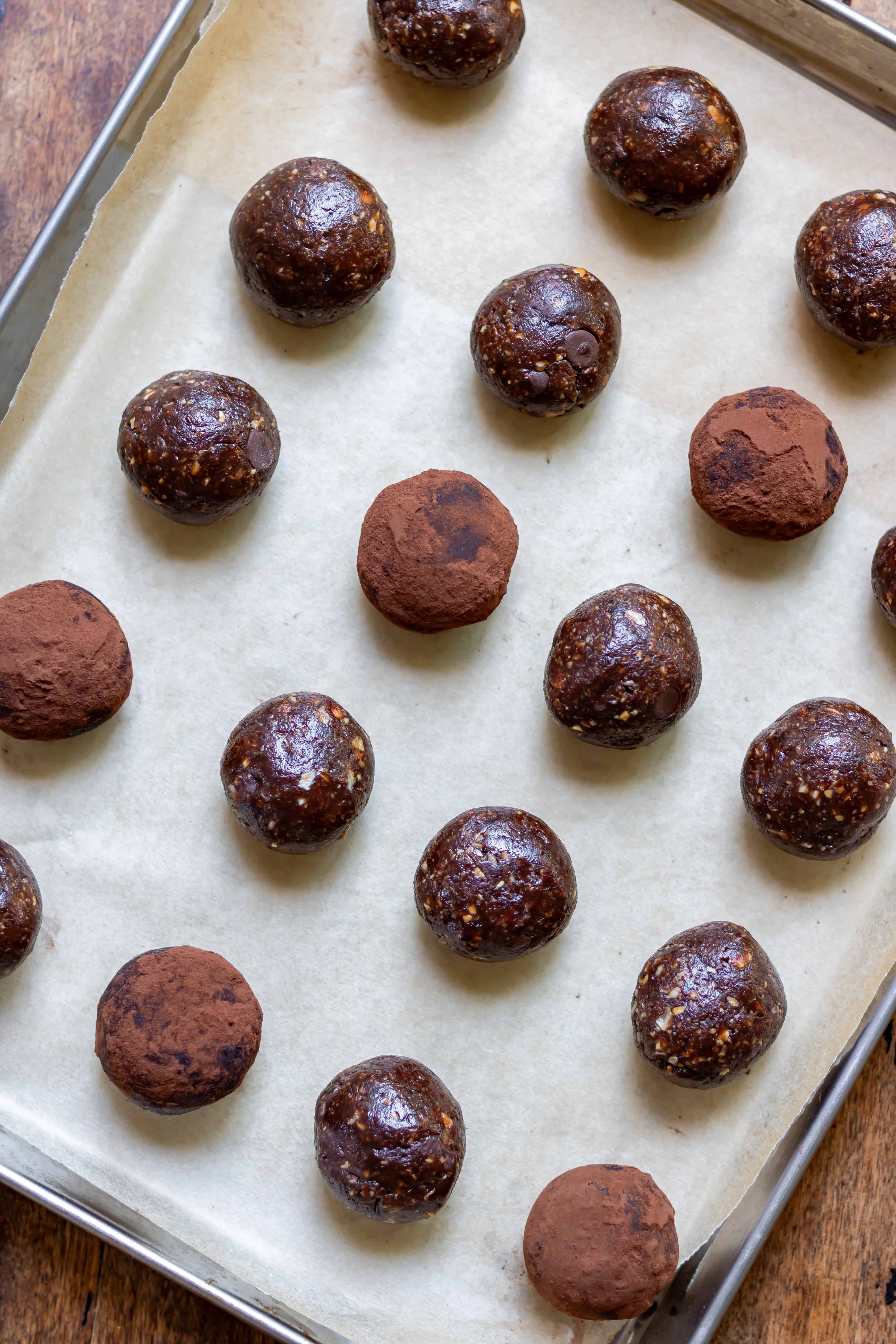 A wooden table with a metal baking sheet of no bake chocolate brownie energy balls.