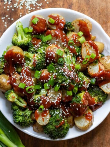 Looking down at a dish of roasted broccoli and potatoes with Korean gochujang sauce, spring onions and sesame seeds.