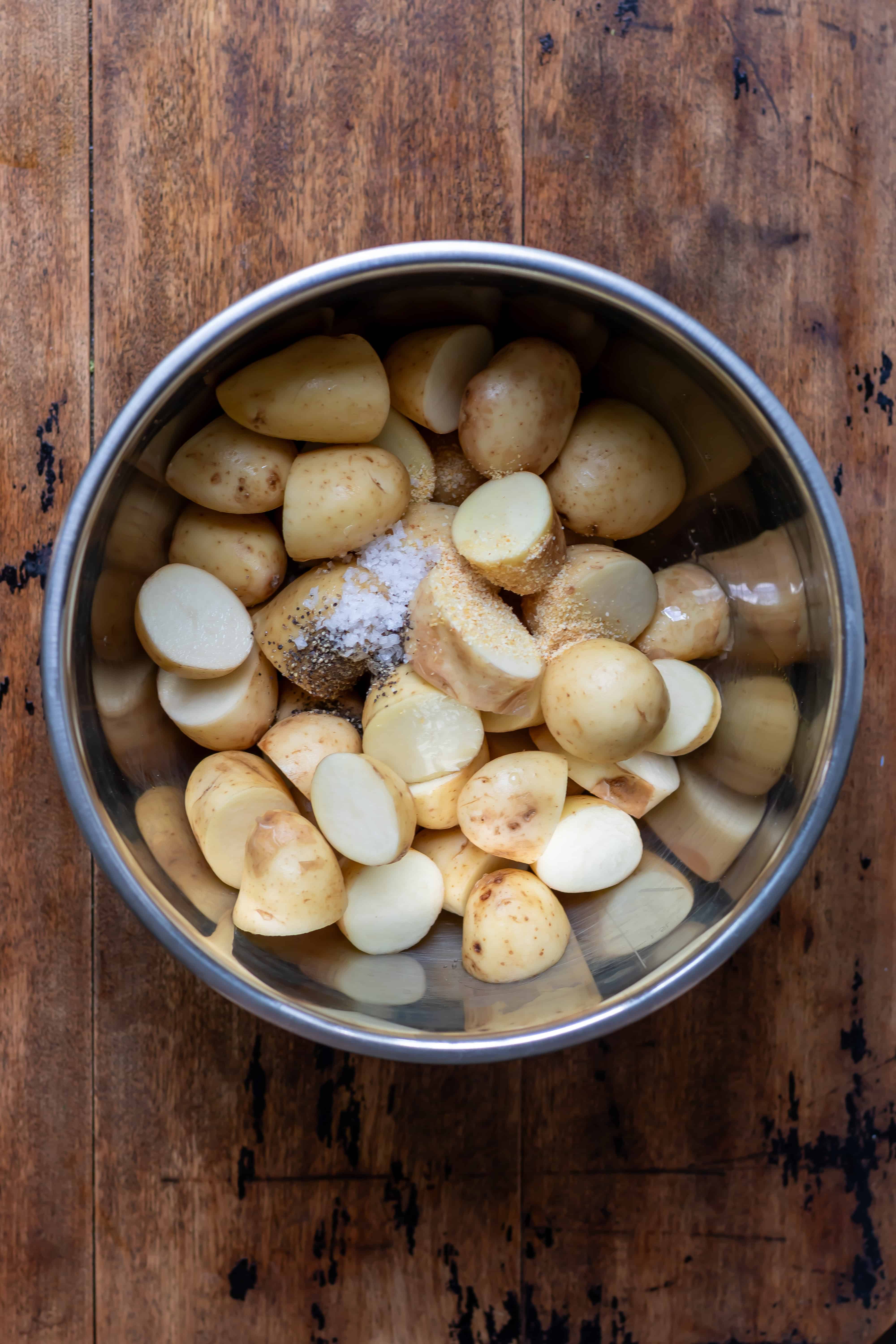 A bowl of halved baby potatoes with salt, pepper and garlic powder.