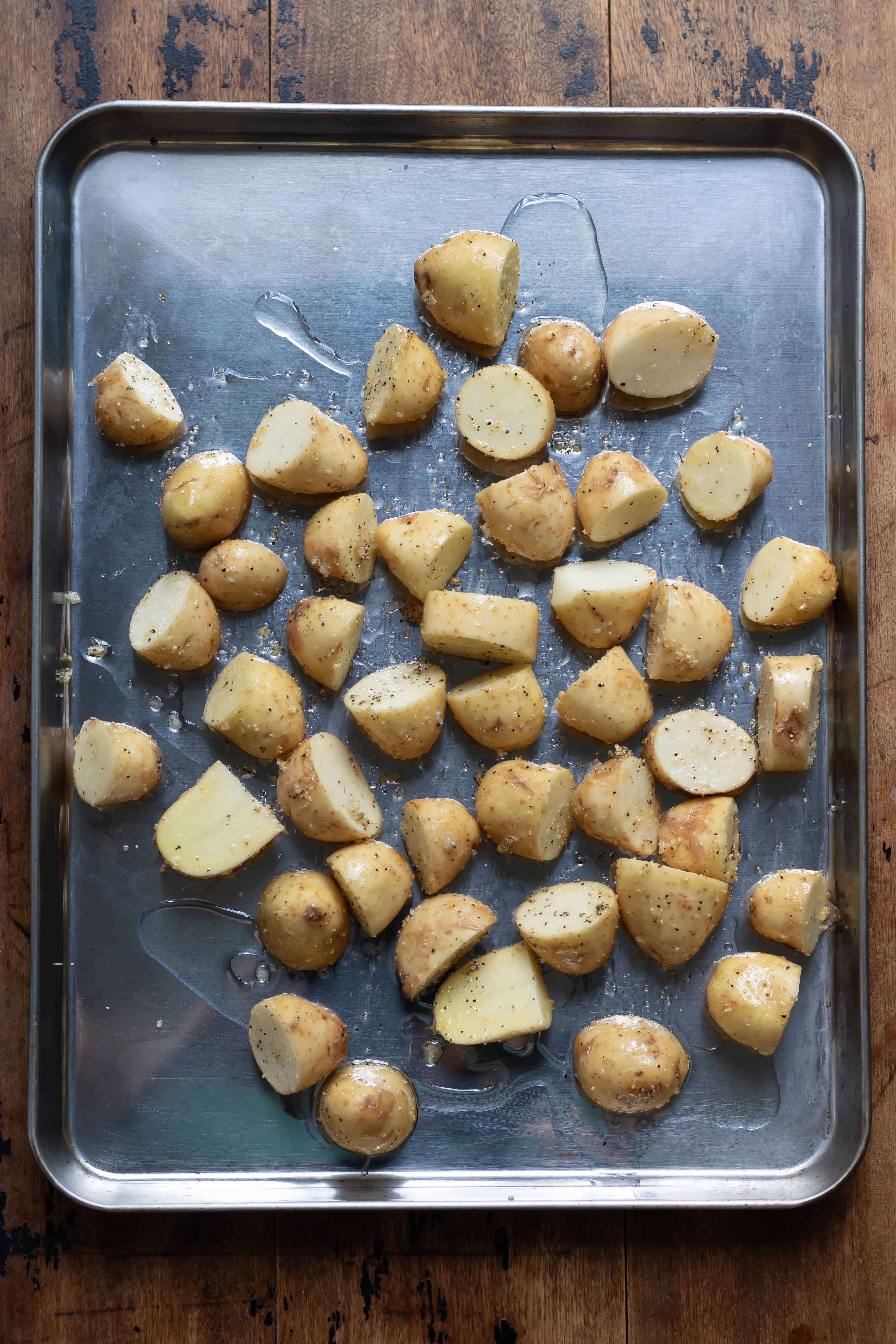 Seasoned halved baby potatoes with oil on a baking sheet.