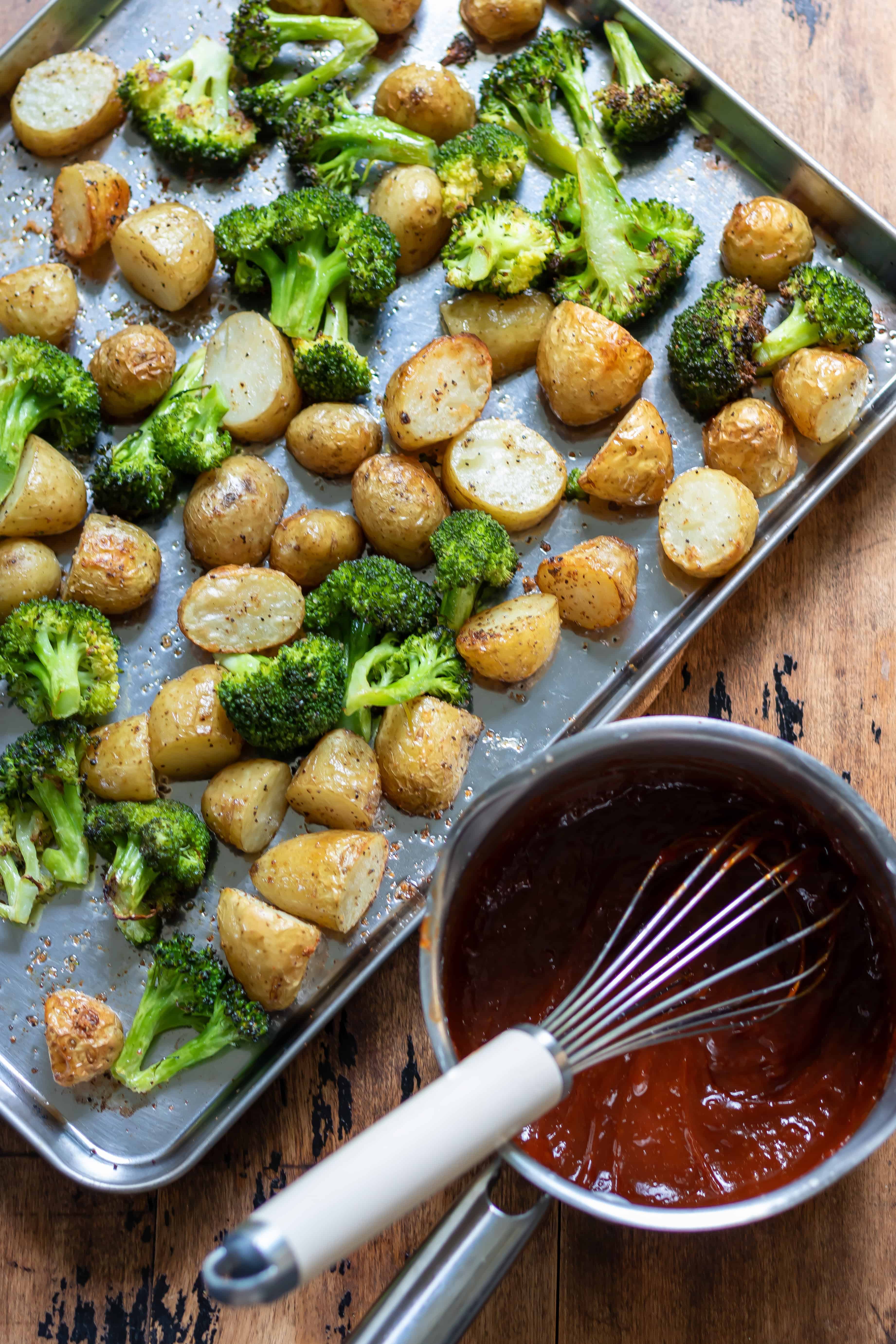 A baking sheet of roasted potatoes and broccoli next to a pot of gochujang sauce.
