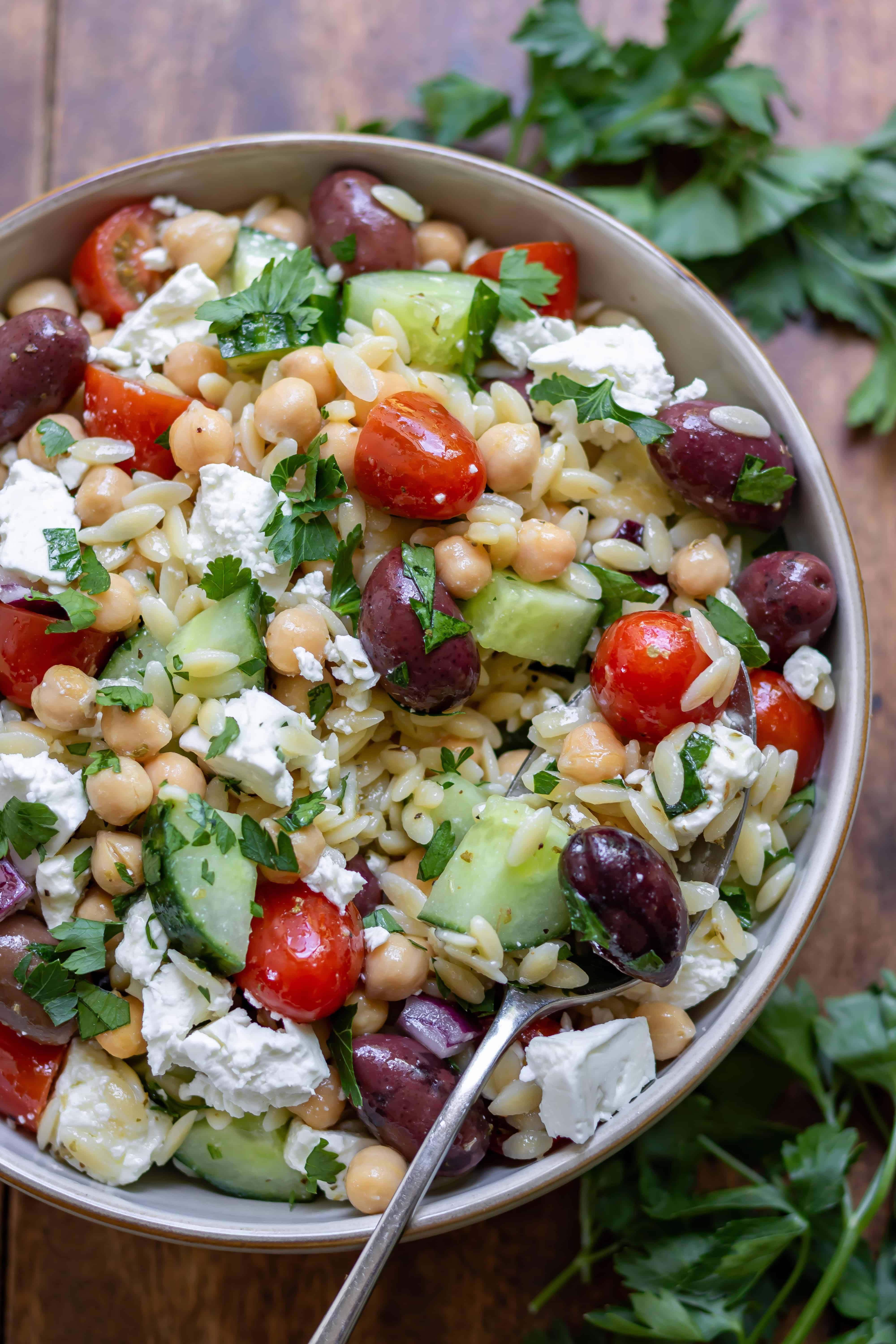Close up of a serving spoon in a dish of Mediterranean Orzo Salad.