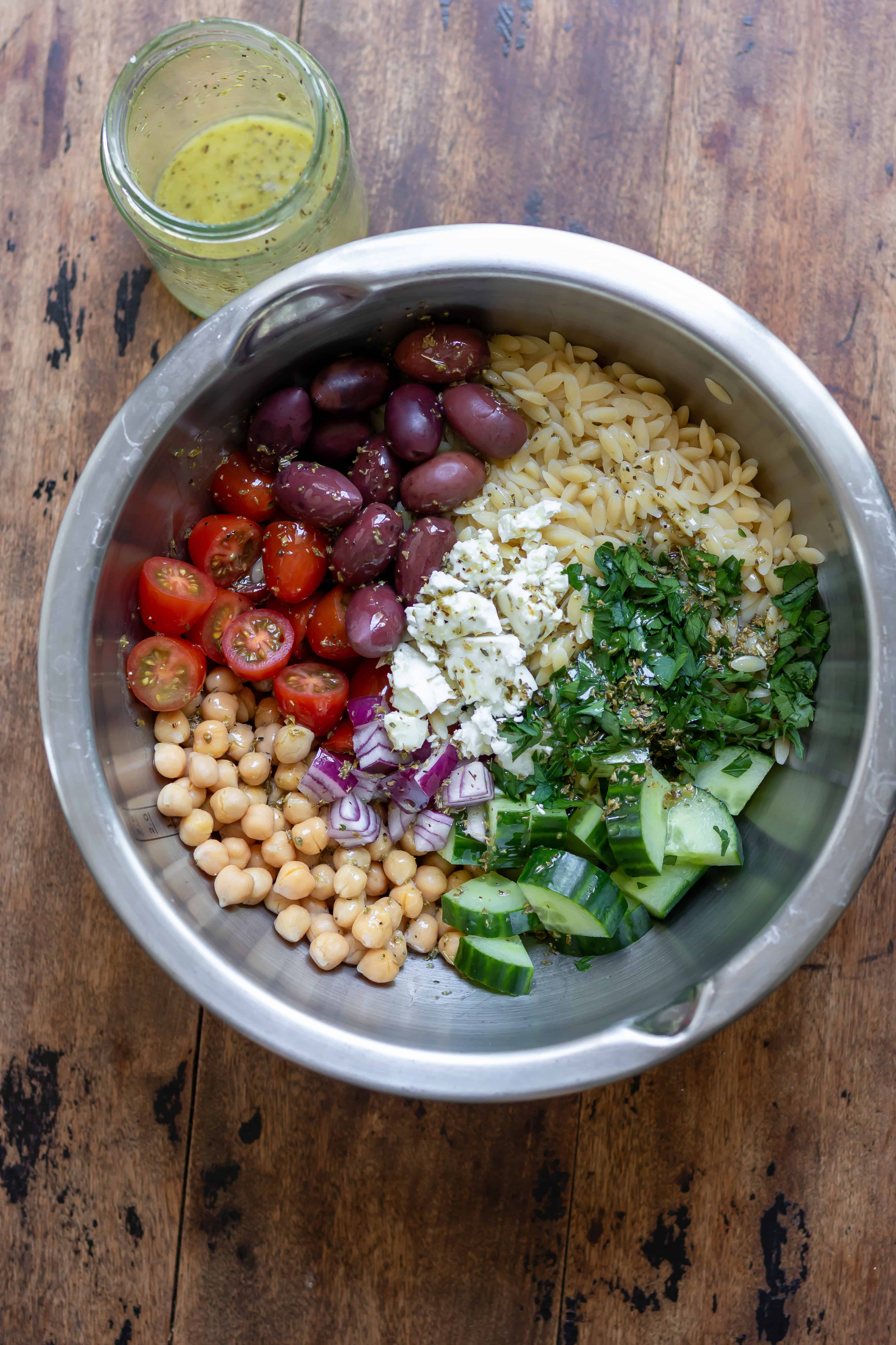 Oregano dressing poured over the veggies and orzo in the mixing bowl.