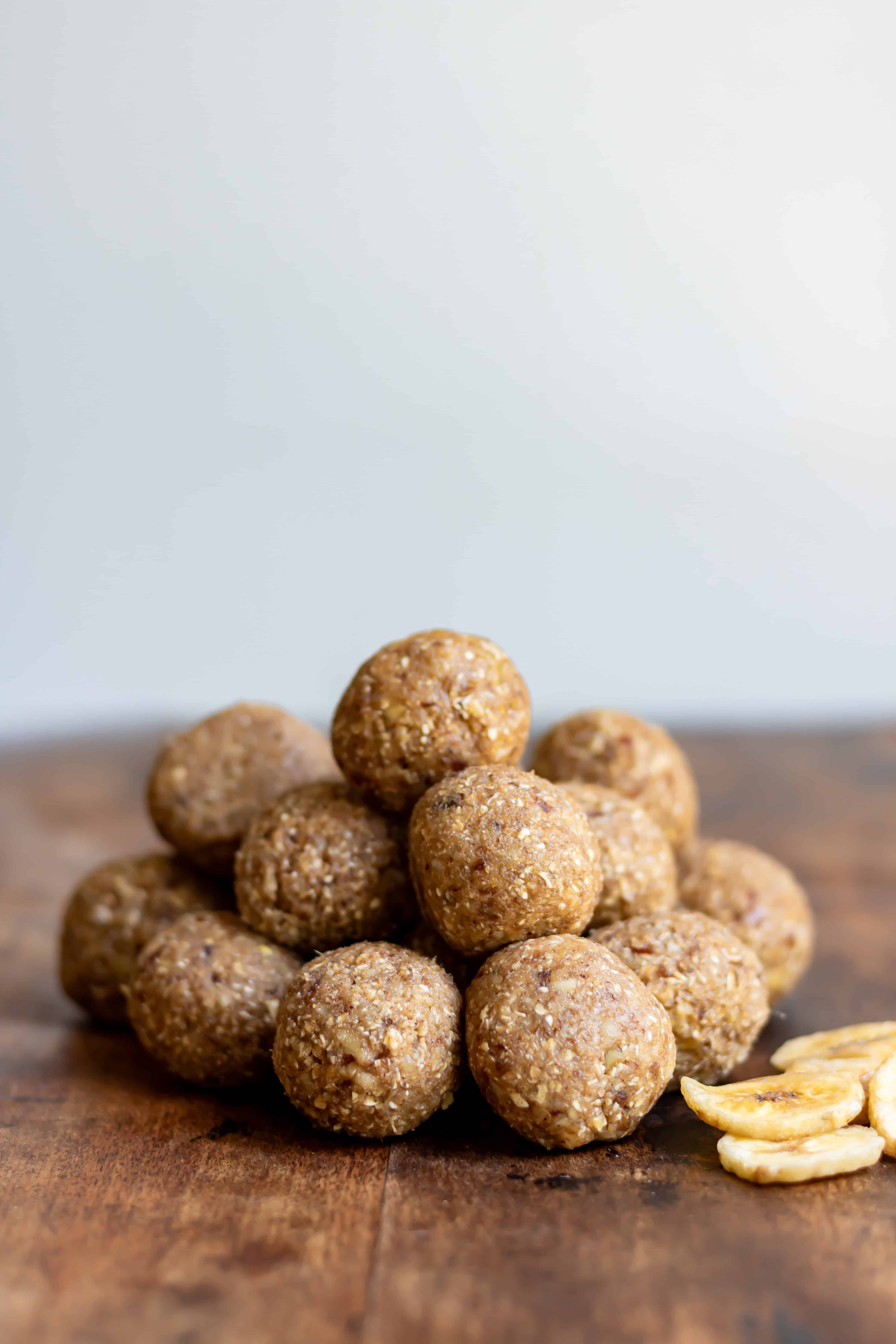 A pile of banana bread protein balls on a wooden table next to dried banana chips.