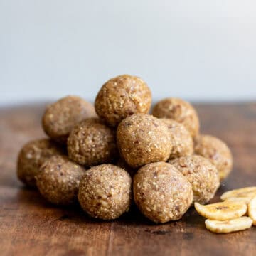 A pile of banana bread protein balls on a wooden table next to dried banana chips.