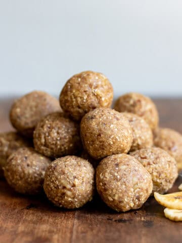 A pile of banana bread protein balls on a wooden table next to dried banana chips.