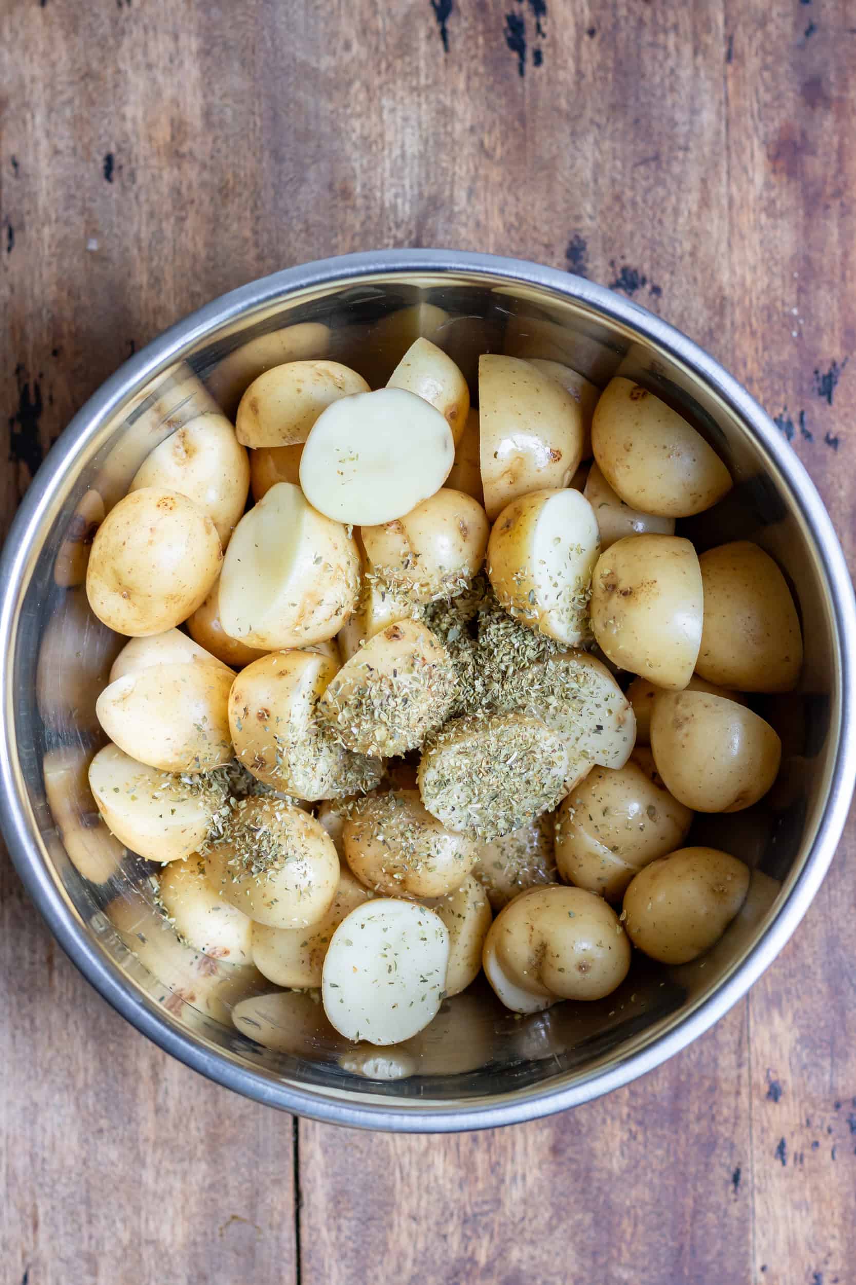 Halved baby potatoes in a bowl with oil and oregano.