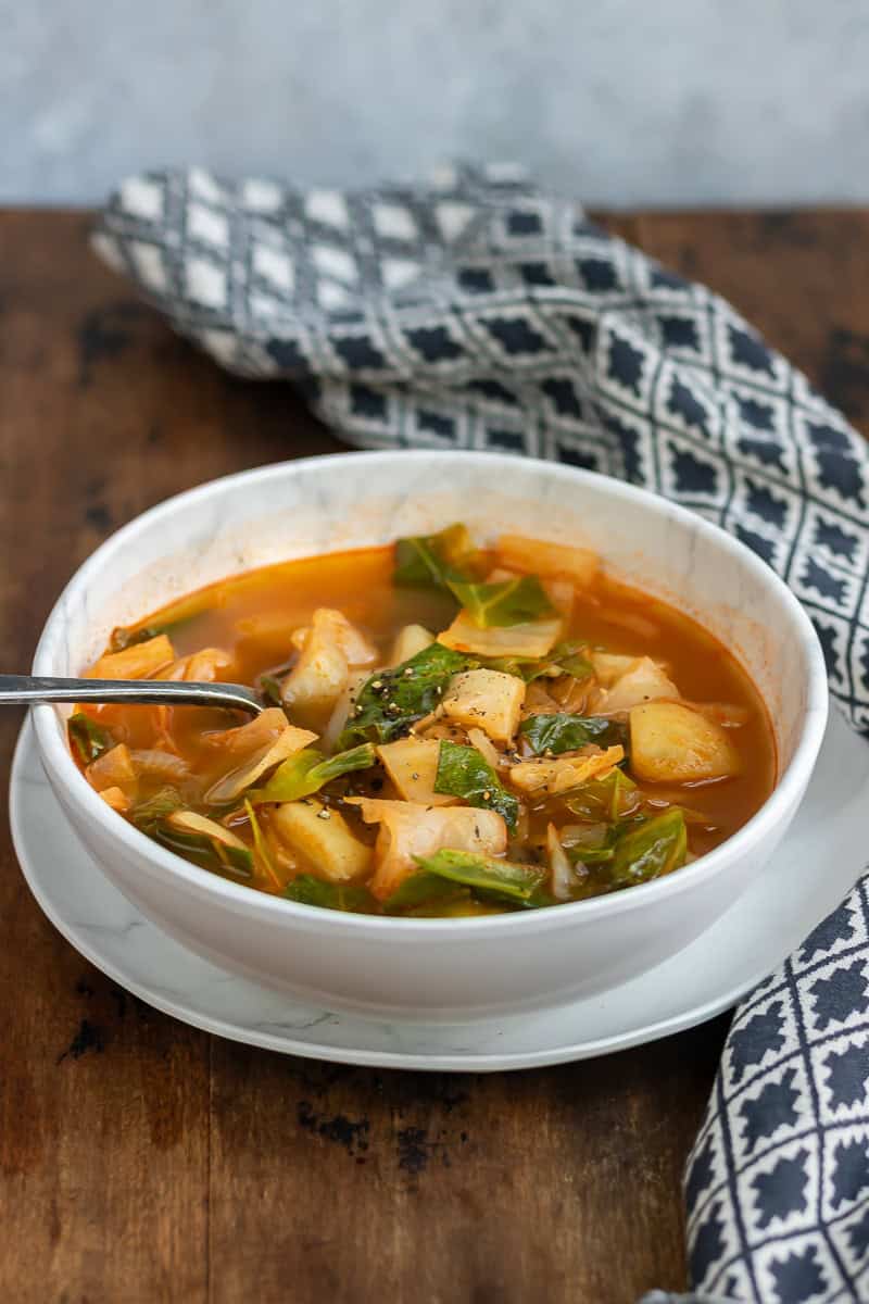 Side view of a table with a bowl of healthy cabbage soup,.
