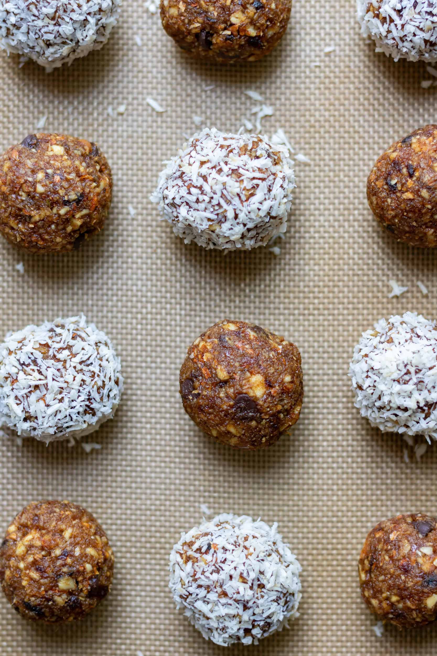 Close up of rows of coconut almond energy balls, with half of them rolled in coconut.