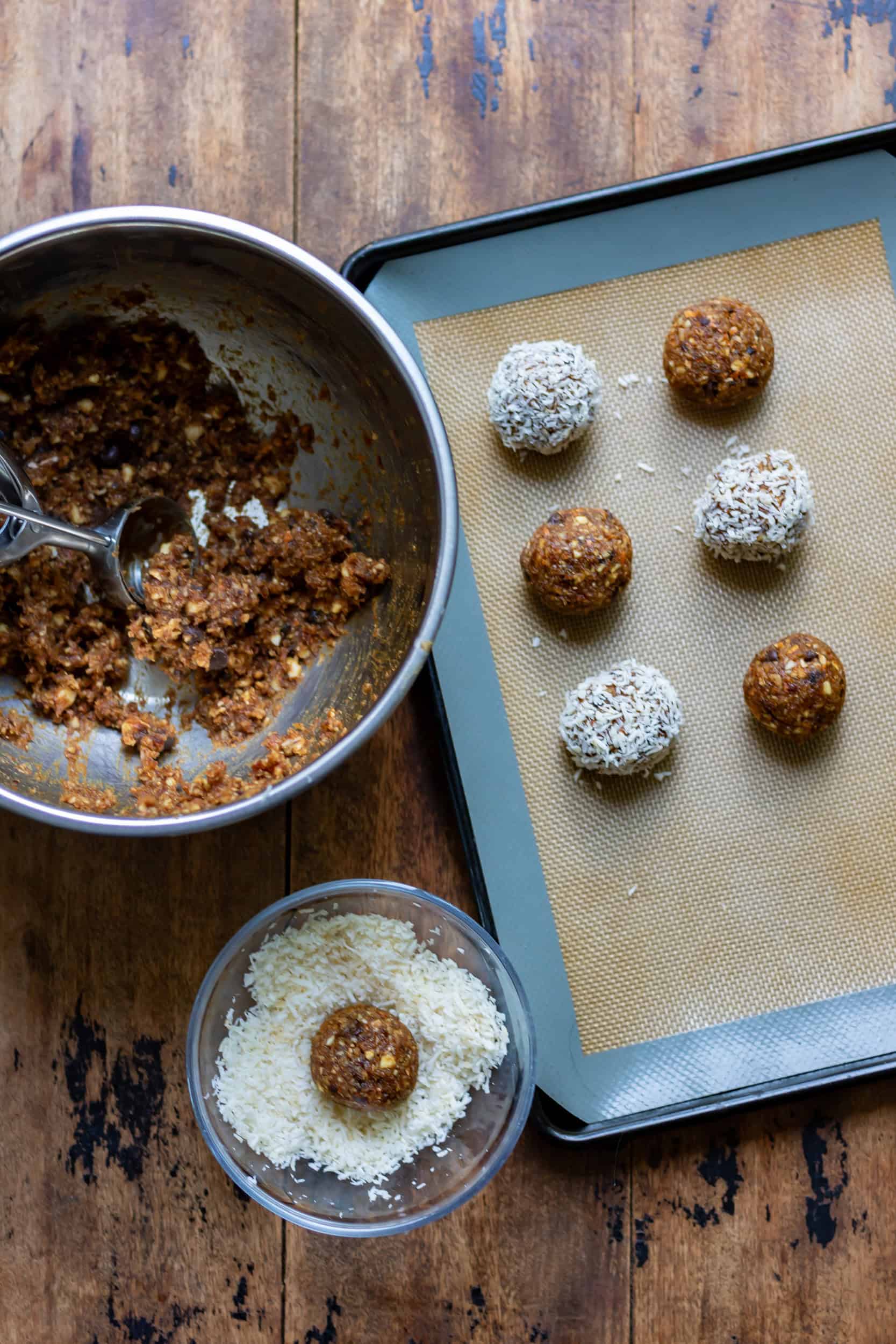 Rolling scoops of coconut almond energy balls into balls and rolling some in coconut.