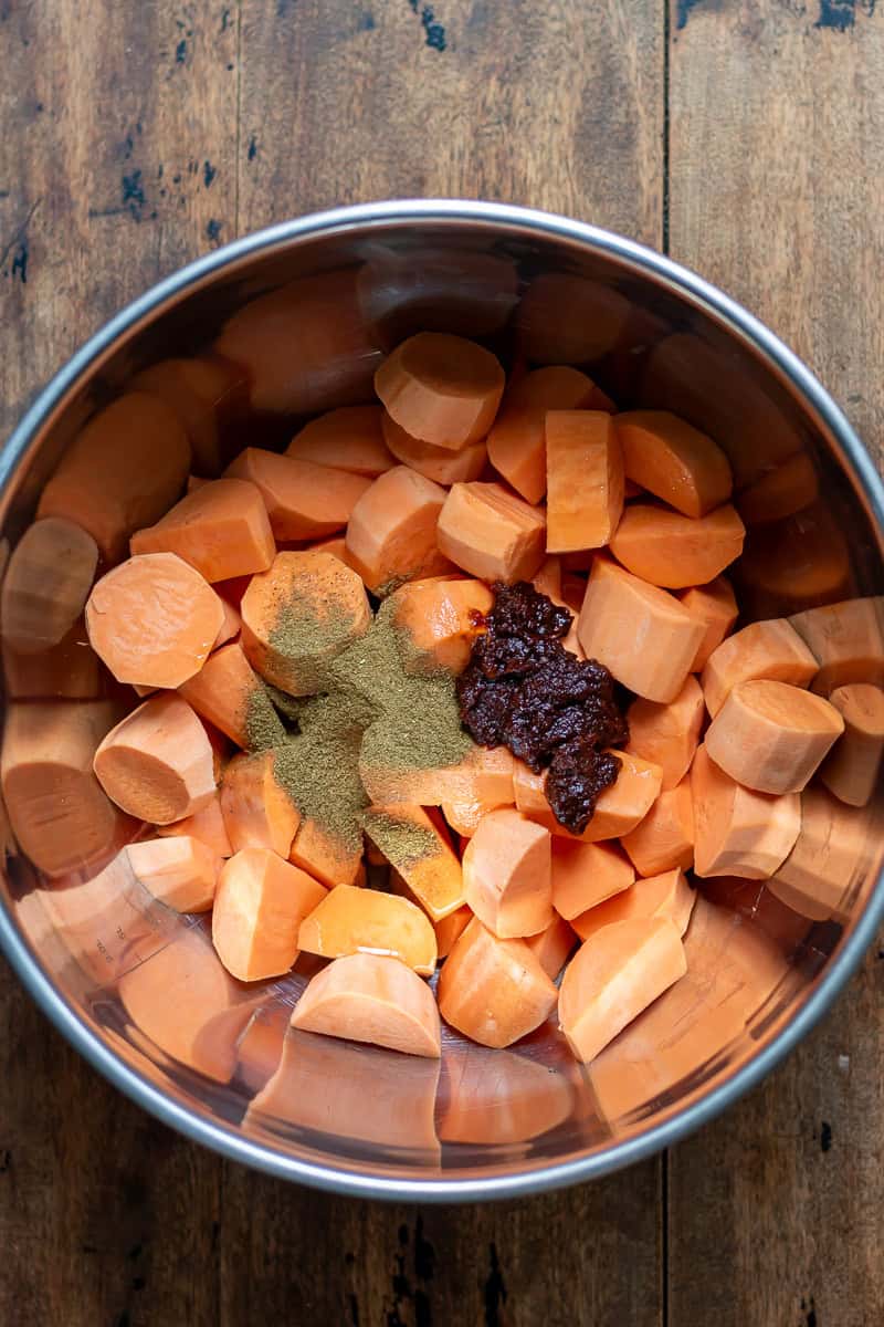 Chipotle and cumin added to a bowl of peeled and chopped sweet potatoes.