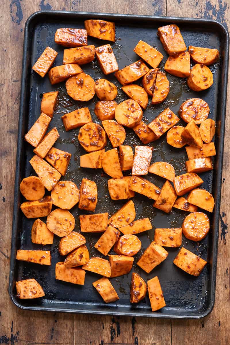 Coated sweet potatoes spread out on a baking sheet.