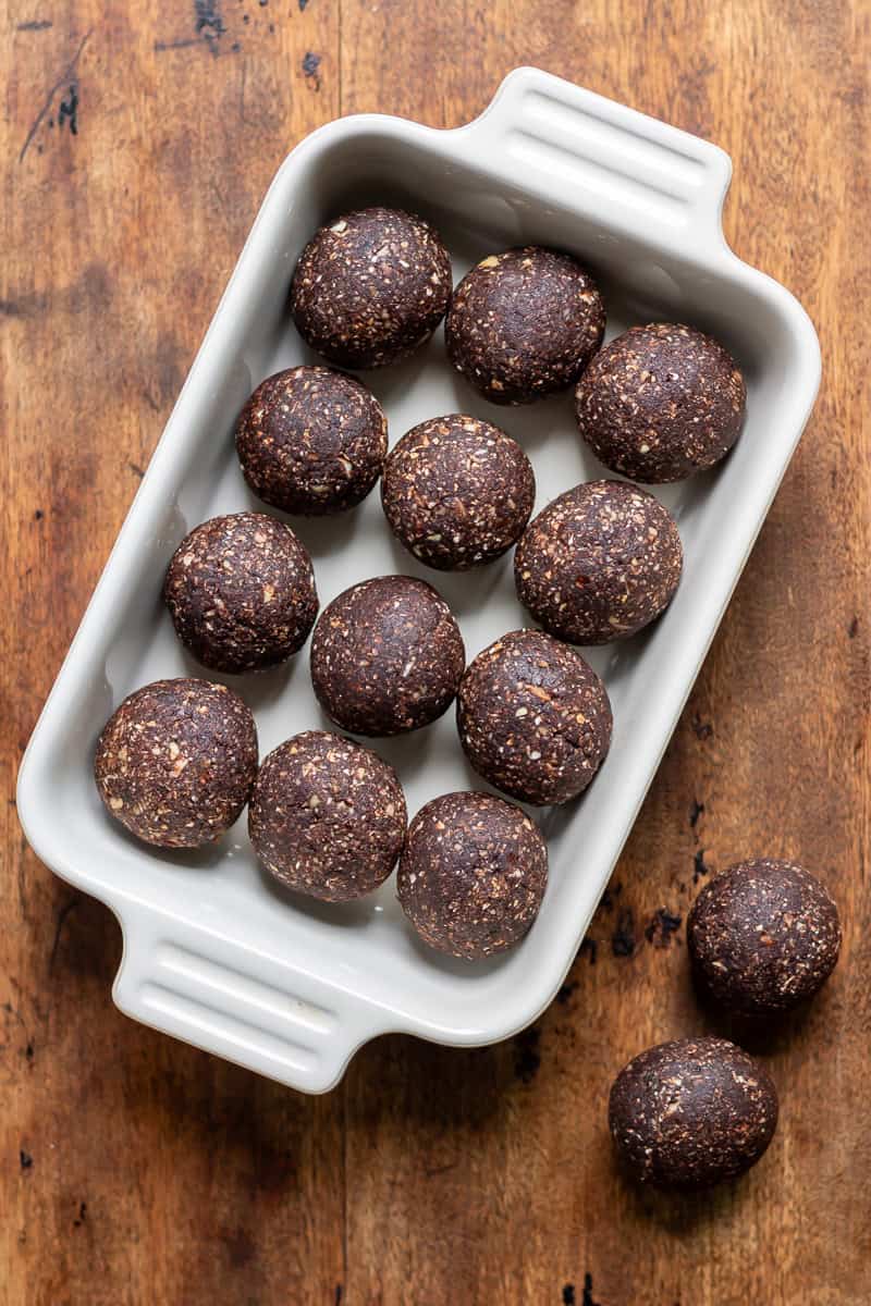 Wooden table with a dish of mint chocolate energy balls, with two on the table next to it.
