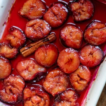 A ceramic dish of roasted plums with a cinnamon stick.