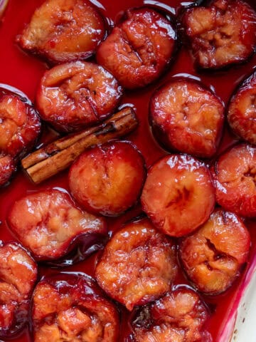 A ceramic dish of roasted plums with a cinnamon stick.